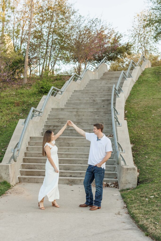 male and female couple pose for Eleanor Tinsley park engagement photos by concrete stairs pretending to dance