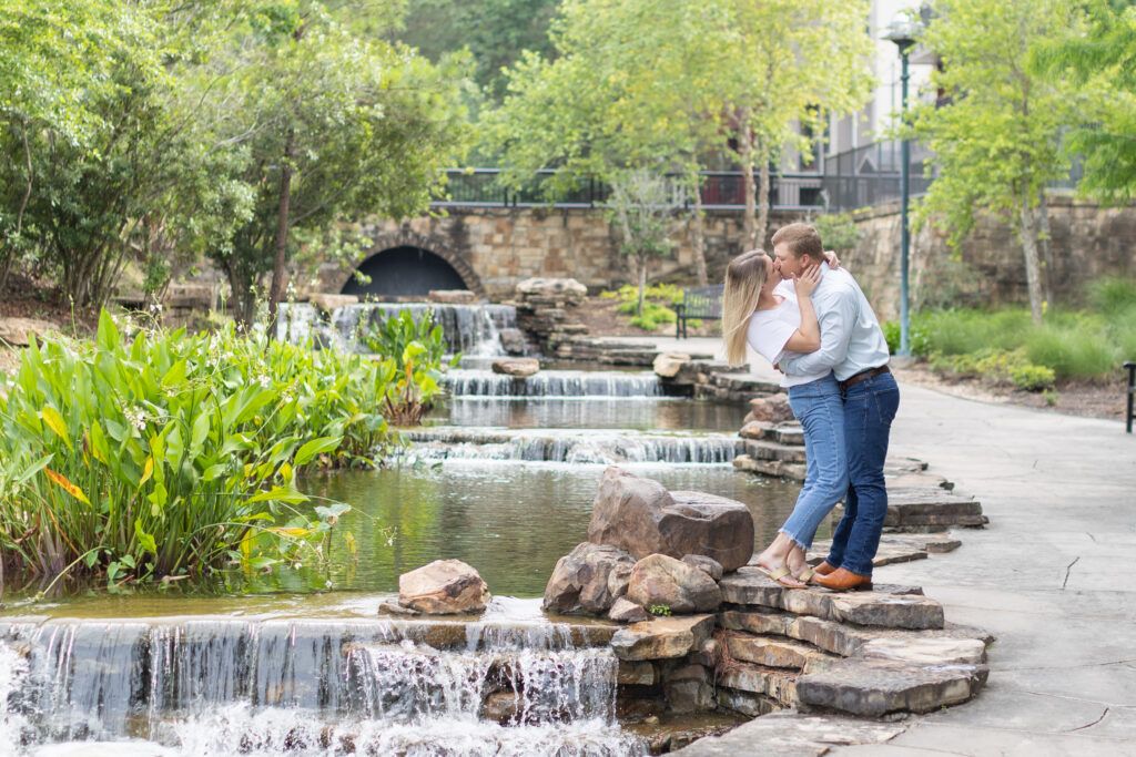 Couple dressed in jeans and white shirts pose for the woodlands engagement photos near a small waterfall