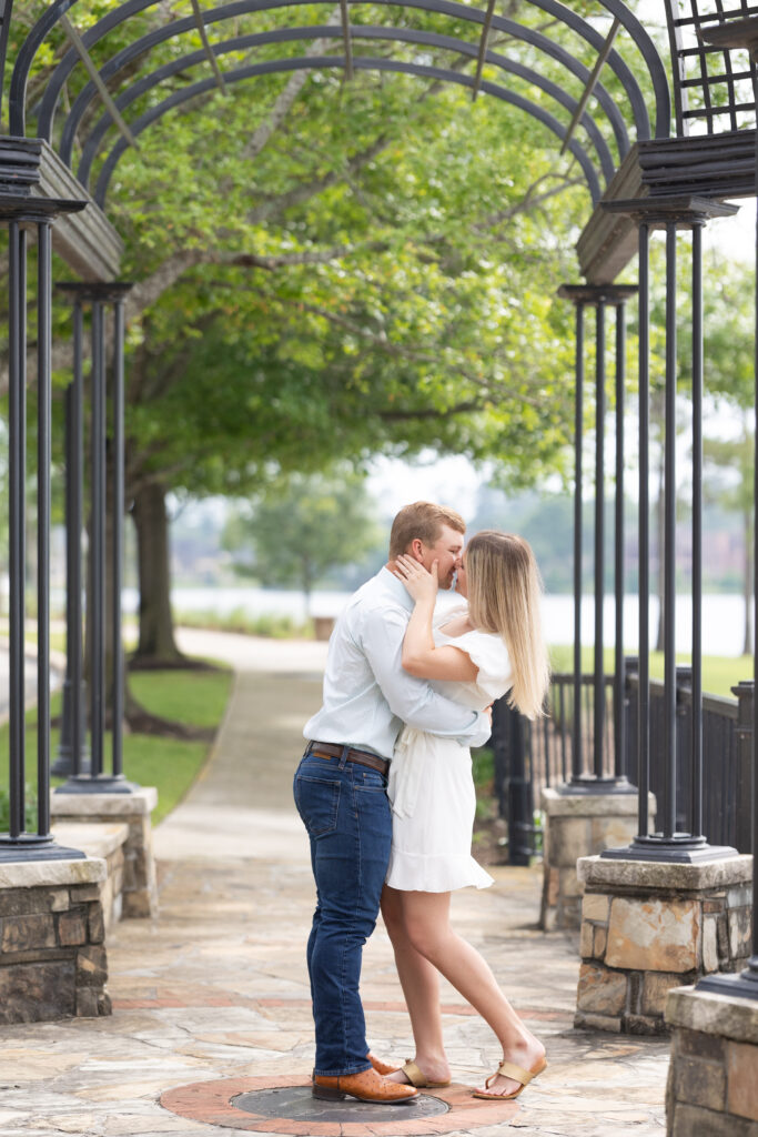 Couple dressed in jeans and white dress pose almost kissing for the woodlands engagement photos under a black iron structure