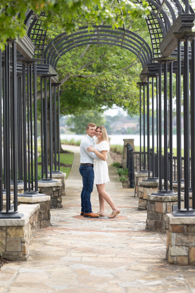 Couple dressed in jeans and white dress pose almost kissing for the woodlands engagement photos under a black iron structure