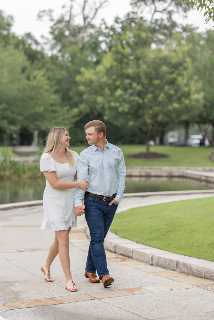 Couple dressed in jeans and white dress walk hand in hand posing for the woodlands engagement photos