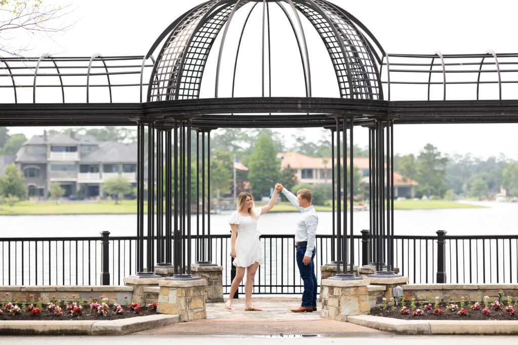 Couple dressed in jeans and white dress pretend to dance for the woodlands engagement photos under a black iron structure